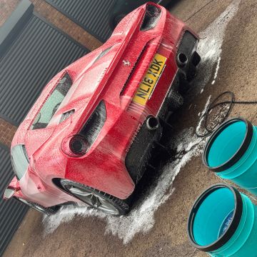 Red Ferrari being washed with soap and water in a driveway.