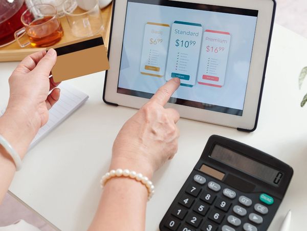 Close-up of a person's hands holding a credit card and pointing at a tablet screen displaying options