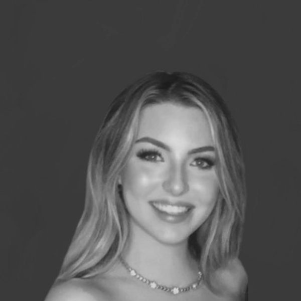 Black and white portrait of a smiling young woman with long, wavy hair, wearing a necklace