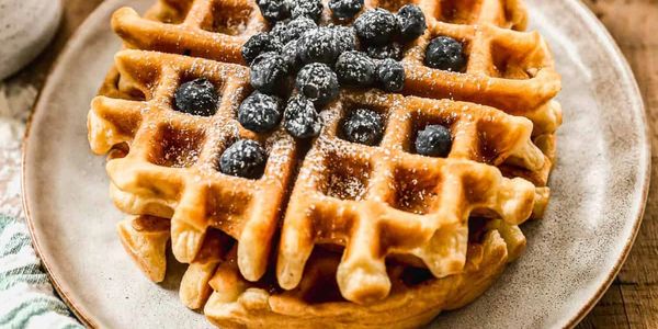 Stack of golden waffles topped with fresh blueberries and powdered sugar.