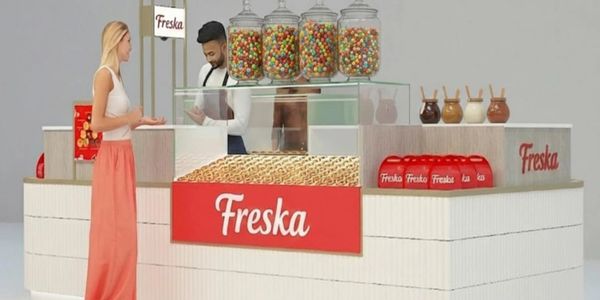 A customer buying snacks at a Freska kiosk with colorful jars and sauces.