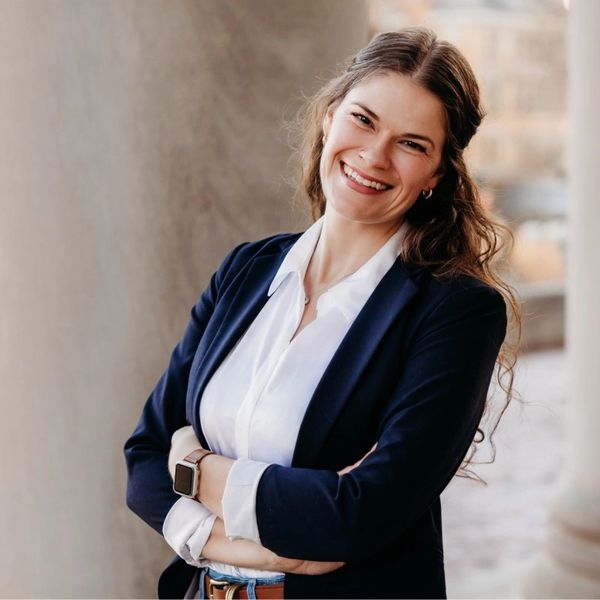 Smiling professional woman in blazer with arms crossed.