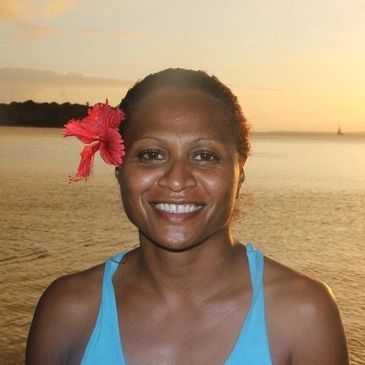 Woman smiling with a red flower in her hair by the water at sunset.