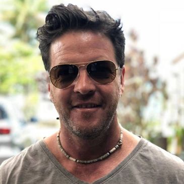 Man wearing sunglasses and a beaded necklace outdoors.