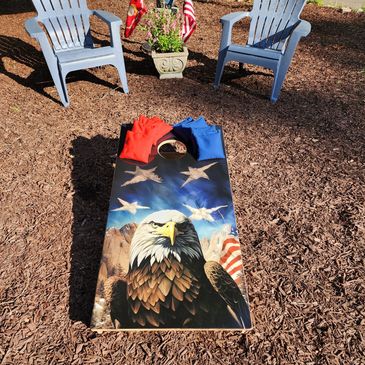 Patriotic cornhole board with eagle design and red and blue bean bags outdoors.