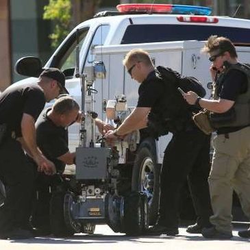 Bomb squad team examining a robotic device near a police vehicle.