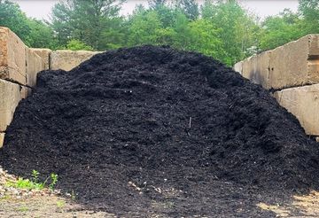 Large pile of dark compost or soil between retaining walls outdoors.