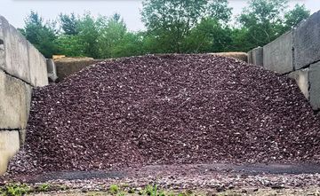 A large pile of crushed purple stones stored between concrete walls outdoors.