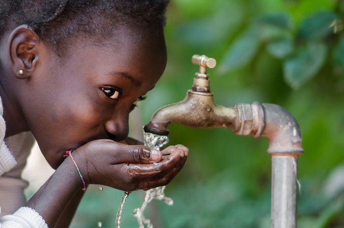 A young girl smiling with the look of joy and hope in her facial expression while drinking water   
