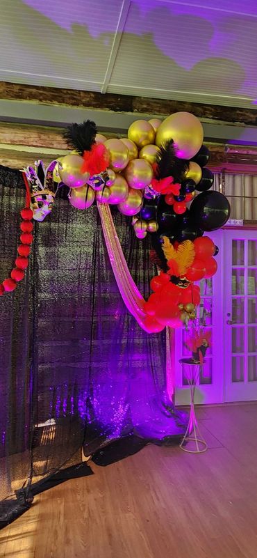 Elegant balloon arch with gold, black, and red colors and feather decorations.