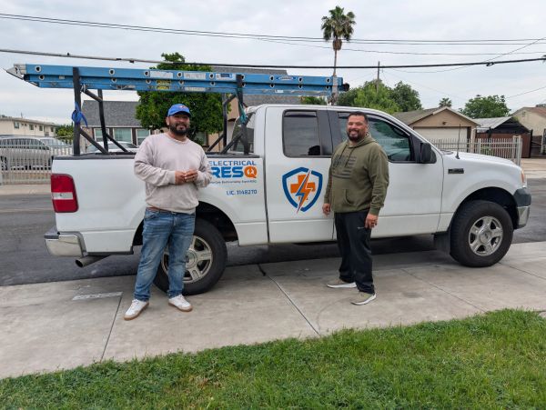 Two men standing beside a white company truck with electrical service logo.