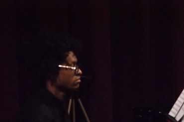 Man playing piano with sheet music in a dimly lit room.