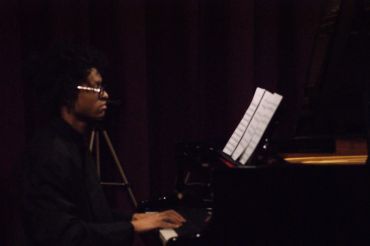 Man playing piano with sheet music in a dimly lit room.