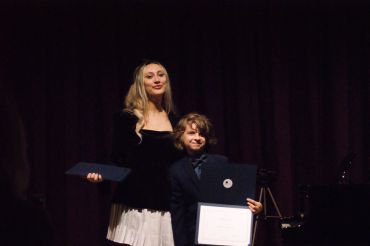 Woman and boy holding diplomas on stage.