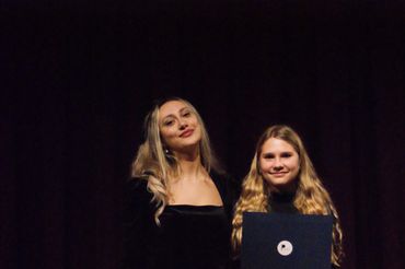 Two young women on stage, one holding a certificate.