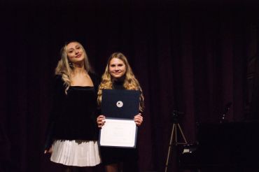 Two young women on stage, one holding a certificate.