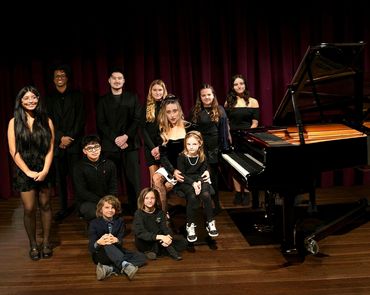 Group of young musicians posing by a grand piano on stage.