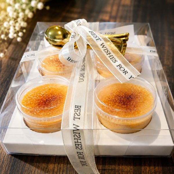 Elegant gift box with four creme brulee desserts and a gold spoon tied with a ribbon.
