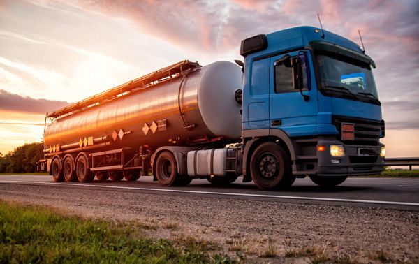 A blue tanker truck driving on a highway at sunset, with a shiny cylindrical tank