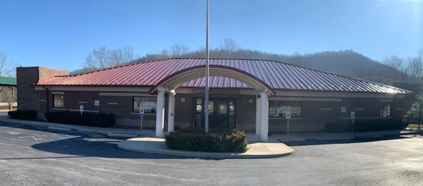 A single-story brick building with a red metal roof and a covered entrance.
