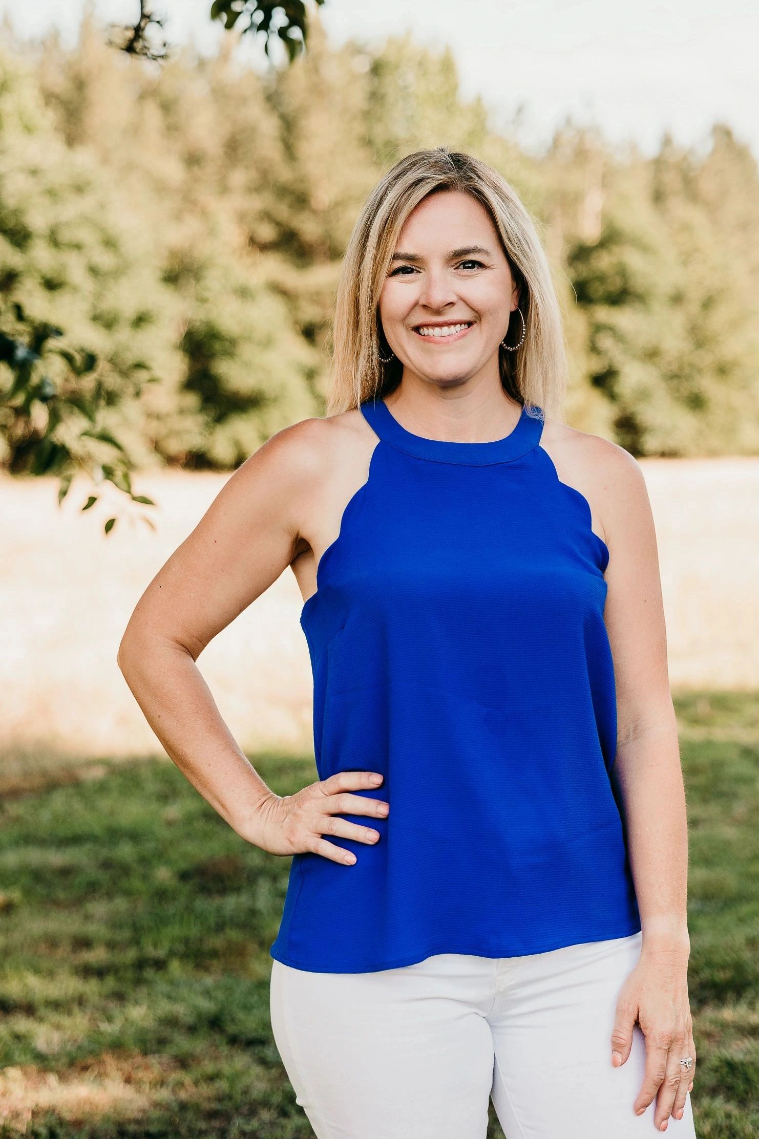 Smiling woman in a blue top and white pants outdoors.
