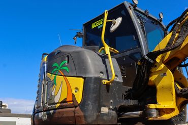 Yellow and black excavator with a palm tree graphic on the side.