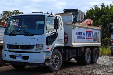 White dump truck parked on a dirt road with signage on its side.