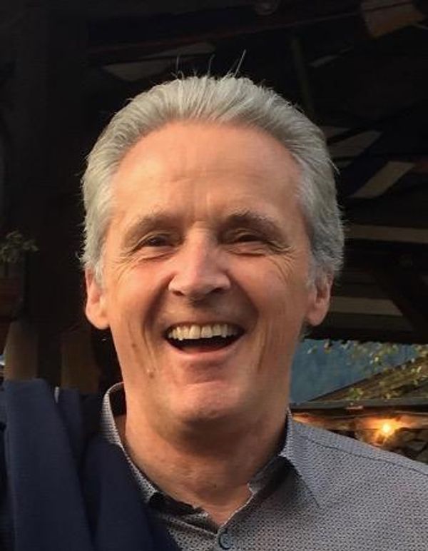 Smiling older man with gray hair outdoors in casual attire.