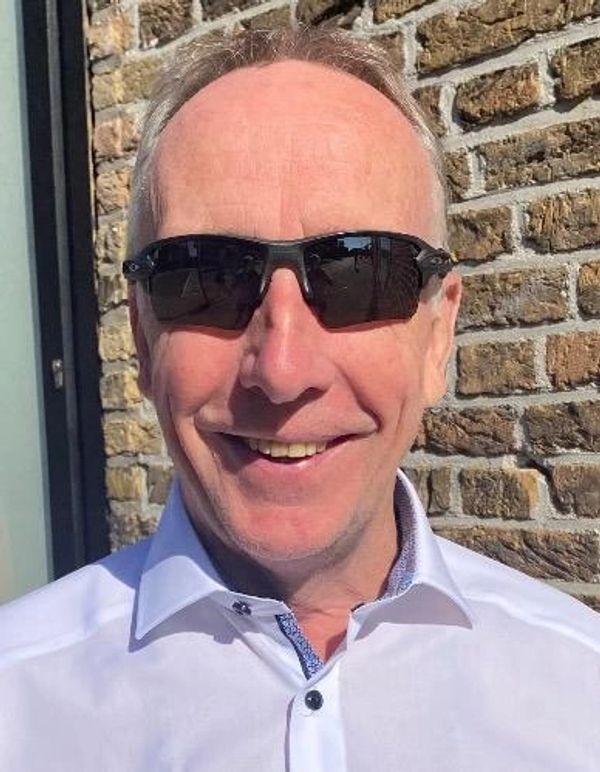 Man wearing sunglasses and a white shirt smiling outdoors.