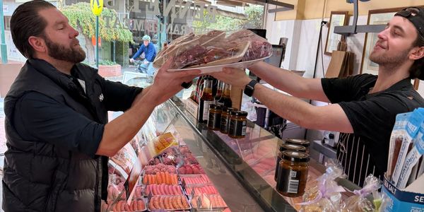 Two men exchanging a large tray of meat at a deli counter.