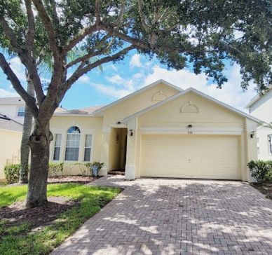 Sunny suburban house with a two-car garage and large tree in front yard.