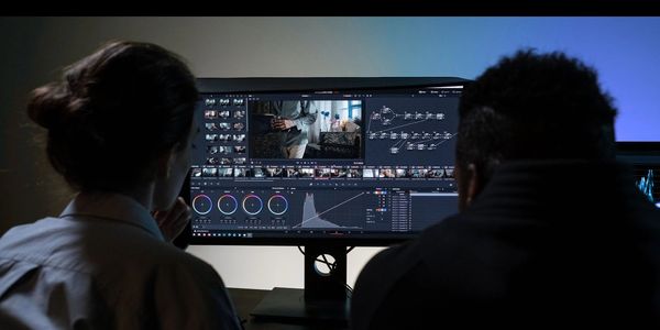 Two people collaborating on video editing and color grading on a computer.