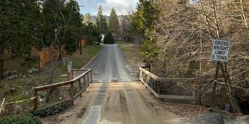 A narrow road bridge with a 5-ton weight limit sign surrounded by trees.