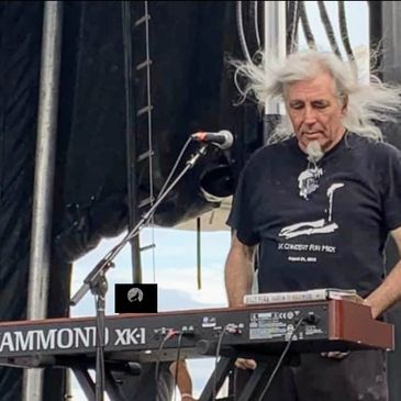 Musician playing a Hammond XK-1 keyboard on stage with long white hair flowing.