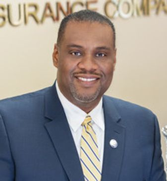 Man in a suit smiling in an office setting.