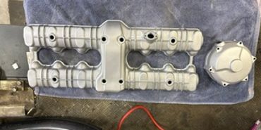 Two silver engine valve covers and a cap on a blue towel.