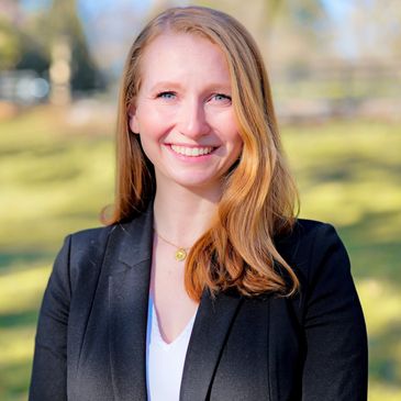 Woman with blonde hair smiling outdoors in a black blazer.