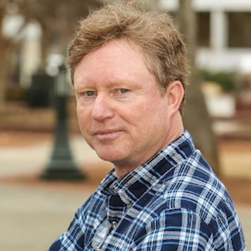 Man with light brown hair in a blue plaid shirt outdoors.
