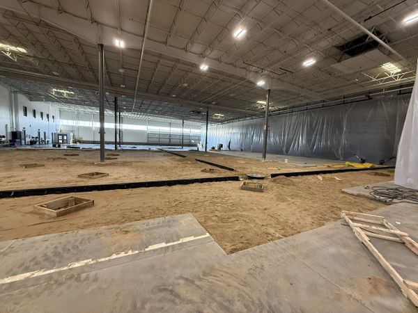 Interior of a large warehouse under construction with exposed dirt and concrete floors.