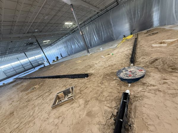 Indoor construction site with trench drains and sand floor preparation.