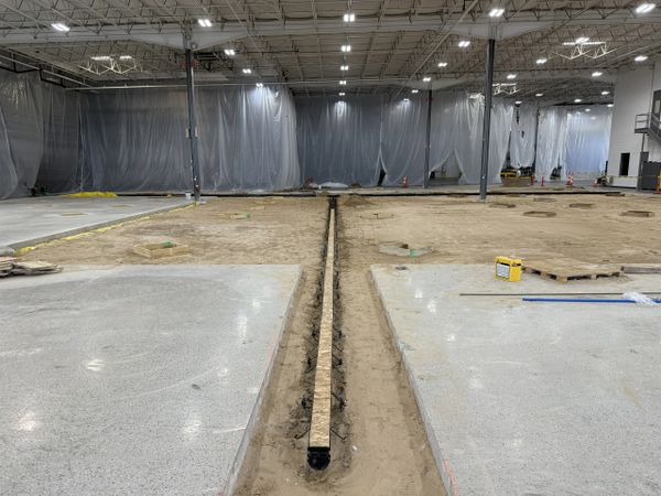 Indoor construction site with trench and concrete slabs under installation.