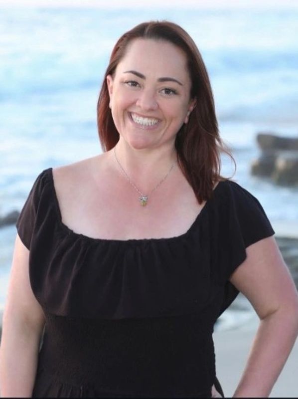 Smiling woman in a black dress at the beach with ocean background.