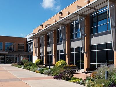 Modern building with large windows and landscaped greenery under a clear sky.