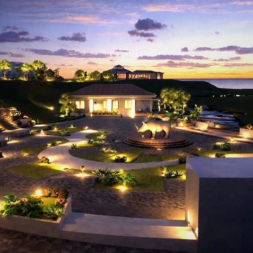 A beautifully lit garden at dusk with a central rhinoceros statue and ocean view.
