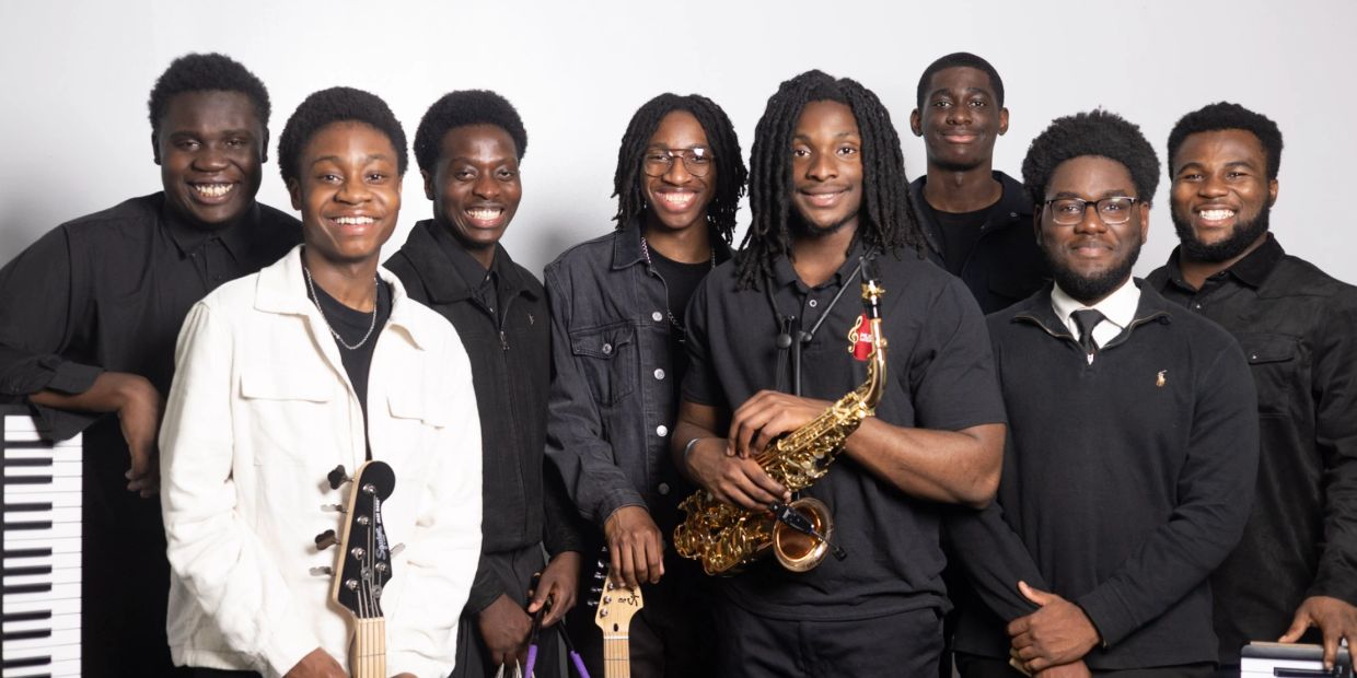 A joyful group of eight young musicians posing with their instruments.