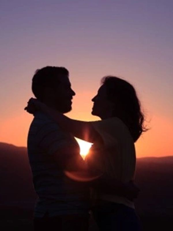 Silhouetted couple embracing at sunset with warm sky.