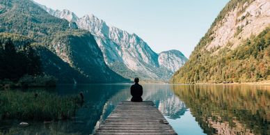 Person sitting on a dock overlooking a serene mountain lake.