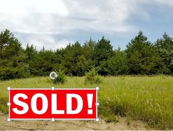A grassy plot of land with a "SOLD!" sign in front.