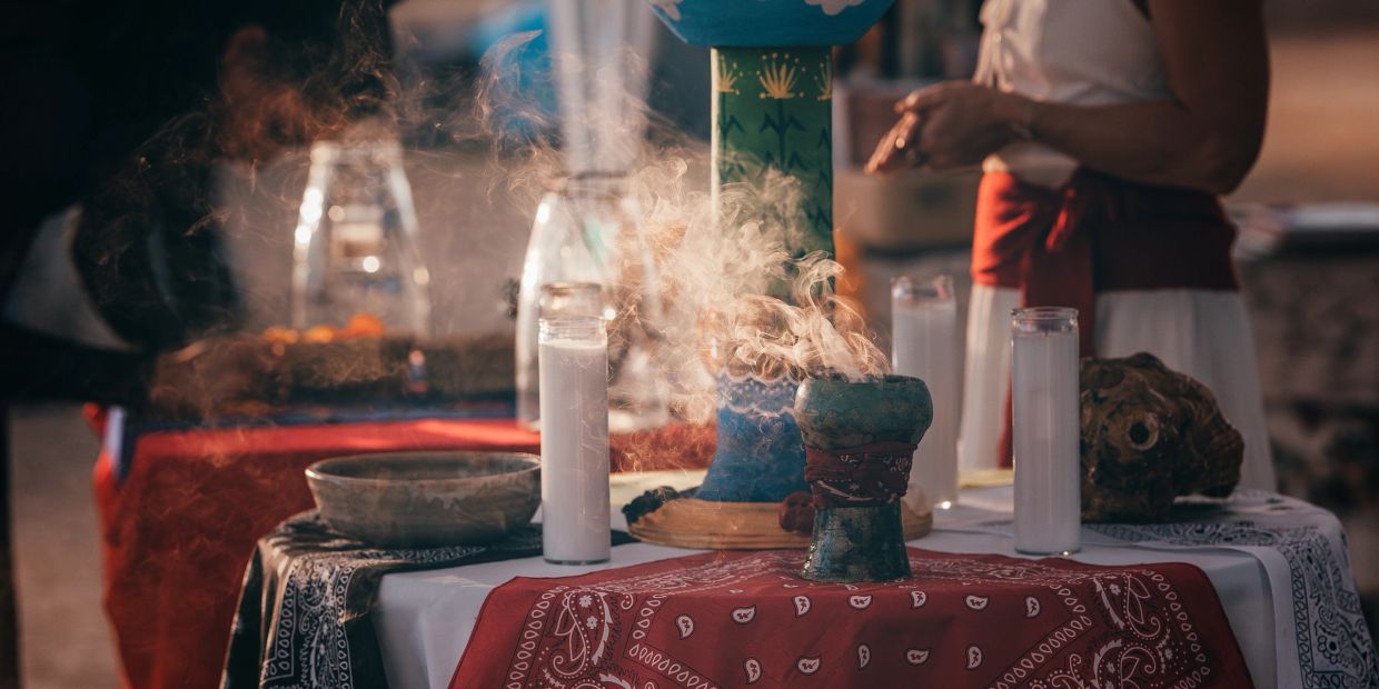 Steaming incense and candles on a decorated altar with a person in the background.