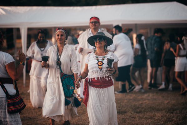People dressed in white at an outdoor gathering, holding cups and smiling.